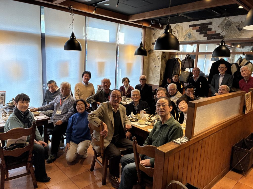 懇親会場、鍛冶屋文蔵千歳橋店の店内での集合写真。多くの人はテーブルについたままカメラの方を向いています。